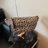 A person holds a leopard print crossbody bag with an adjustable strap against a light background.