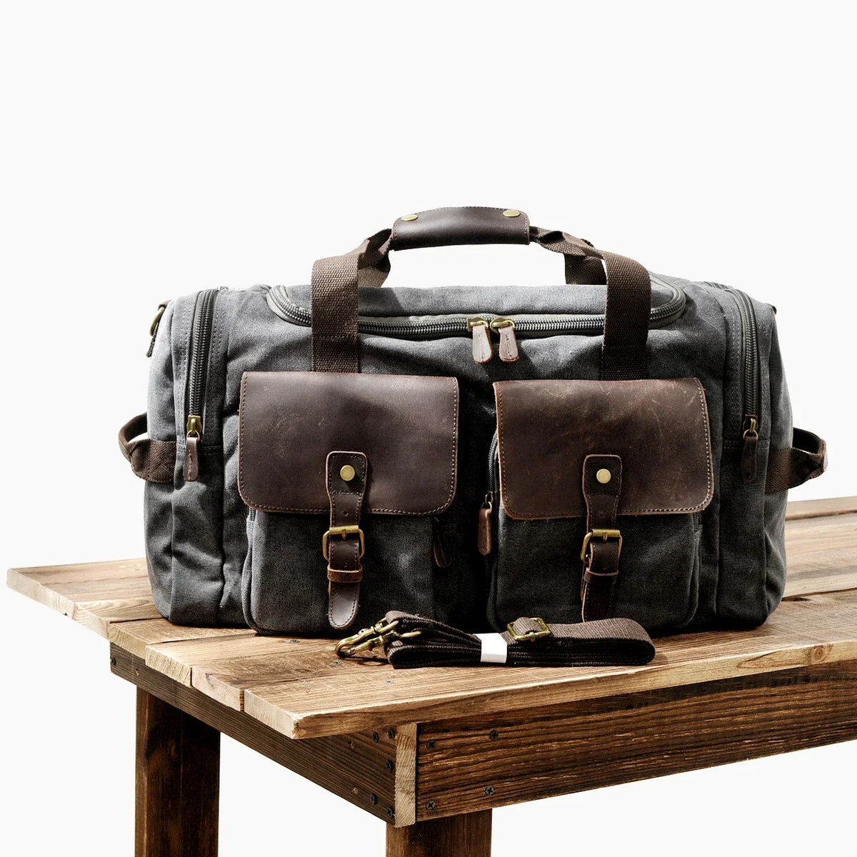 Dunkelgrabe Reise-Gepäcktasche aus Canvas mit braunen Lederakzenten auf Holzoberfläche.
