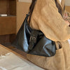 A woman holds a black PU leather underarm bag in a tan jacket, resting on a glass surface.