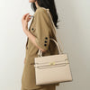 A woman wearing a beige blazer holds a light beige luxury handbag.