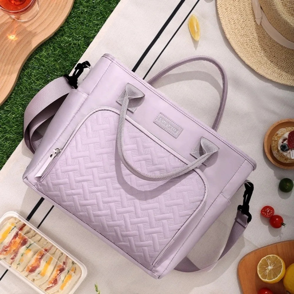 A light purple quilted insulated lunch bag resting on a white surface with fruit and a straw hat.