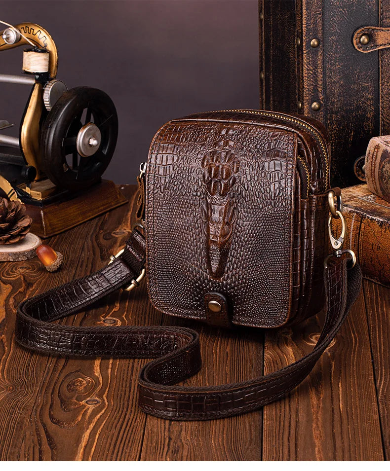 A dark brown genuine cow leather crossbody bag with a crocodile texture resting on a wooden surface.