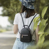 A woman wearing a white t-shirt and denim overalls carries a black waterproof PU mini backpack outdoors.