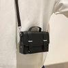 A black minimalist leather crossbody bag is shown hanging on a white shirt.
