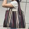 A person is holding a brown and beige striped foldable grocery tote bag against a light gray wall.