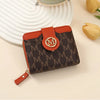 An orange leather compact wallet with a brown monogram pattern rests on a light surface.