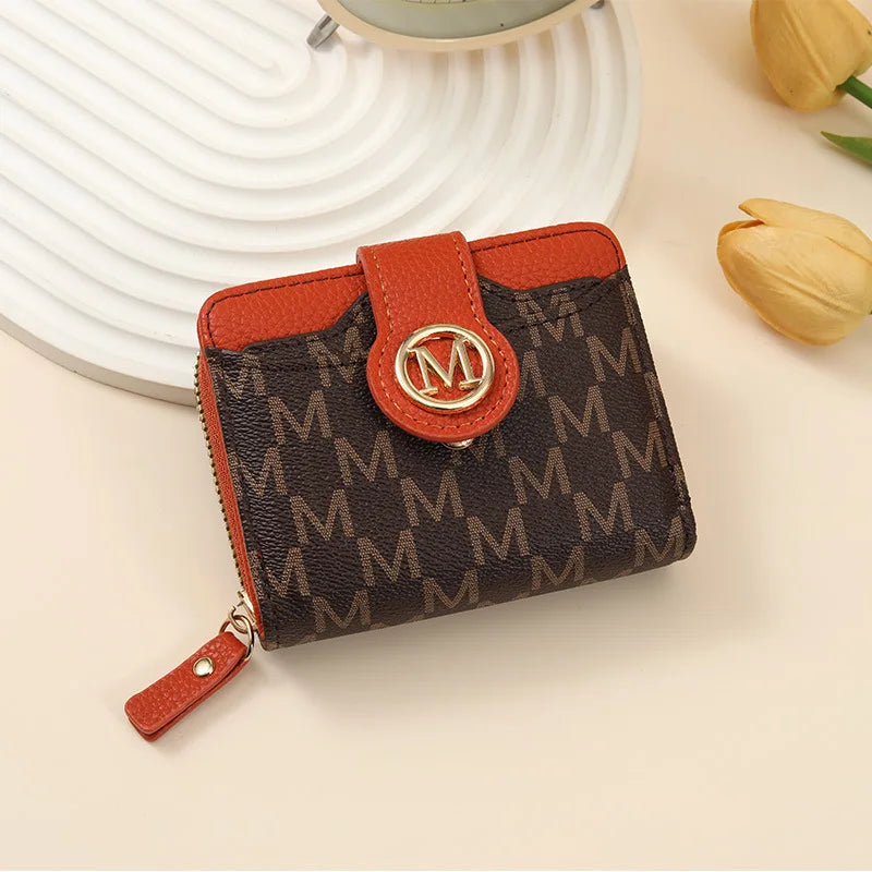 An orange leather compact wallet with a brown monogram pattern rests on a light surface.