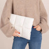 Une personne tient une housse de sac d'ordinateur rembourrée blanche contre un pull beige et un jean bleu.