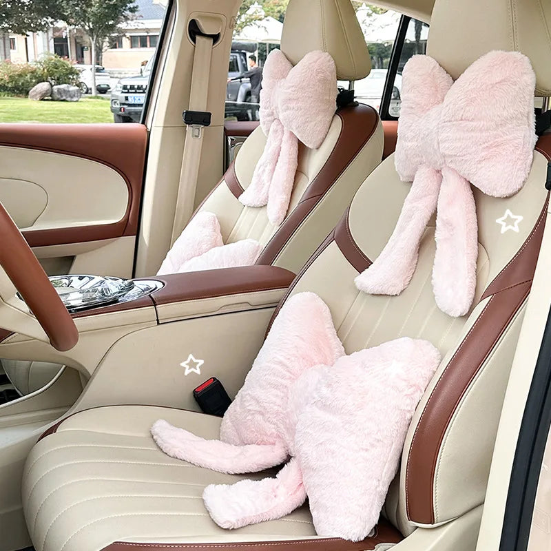 Interior view of a car seat showing pink bowknot headrest pillows and lumbar support cushions.