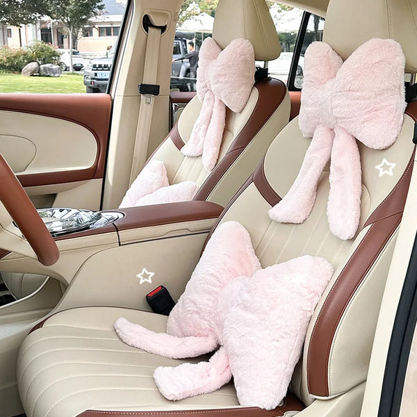 Interior view of a car seat showing pink bowknot headrest pillows and lumbar support cushions.