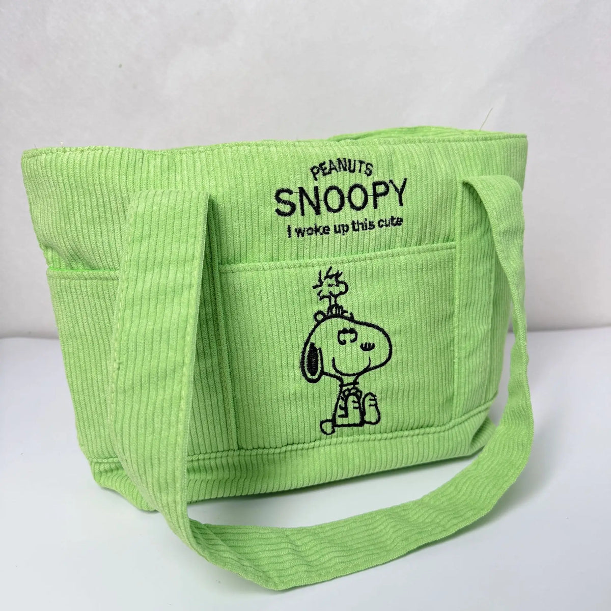 A lime green canvas shoulder bag featuring a Snoopy cartoon design.