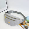 A light gray nylon crossbody fanny pack with a gold zipper and leather accent resting on a white surface.