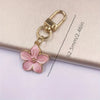 A pink resin flower keychain with a gold-colored clasp and jump ring attached to a light beige surface.