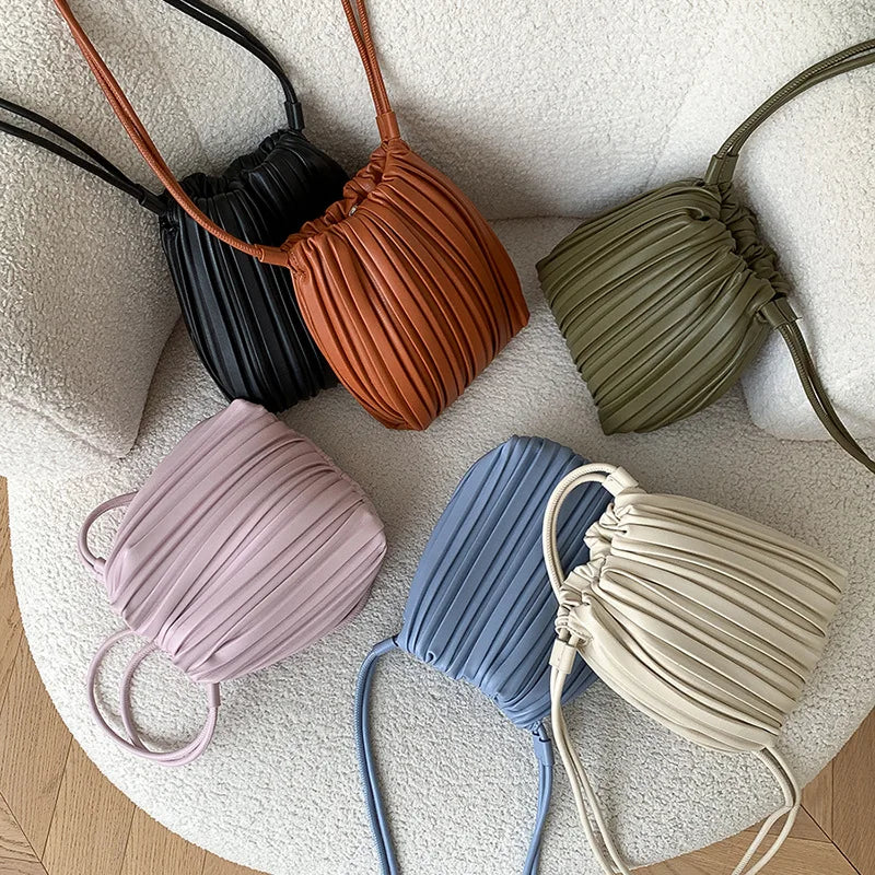 A collection of nine PU leather pleated crossbody bags in shades of black, terracotta, olive green, mauve, blue, and beige.