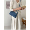 A woman wearing a cream knit dress holds a navy blue faux suede crossbody bag and a book.