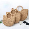 A handwoven rattan beach bag with a wide brim and a loop handle, displayed on a white surface.
