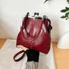 A deep burgundy leather handbag with a silver frame and strap is held by a person against a white background.