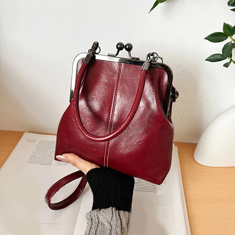 A deep burgundy leather handbag with a silver frame and strap is held by a person against a white background.
