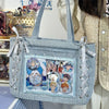 A light blue textured canvas tote bag with white ribbon details and a transparent window featuring various character illustra