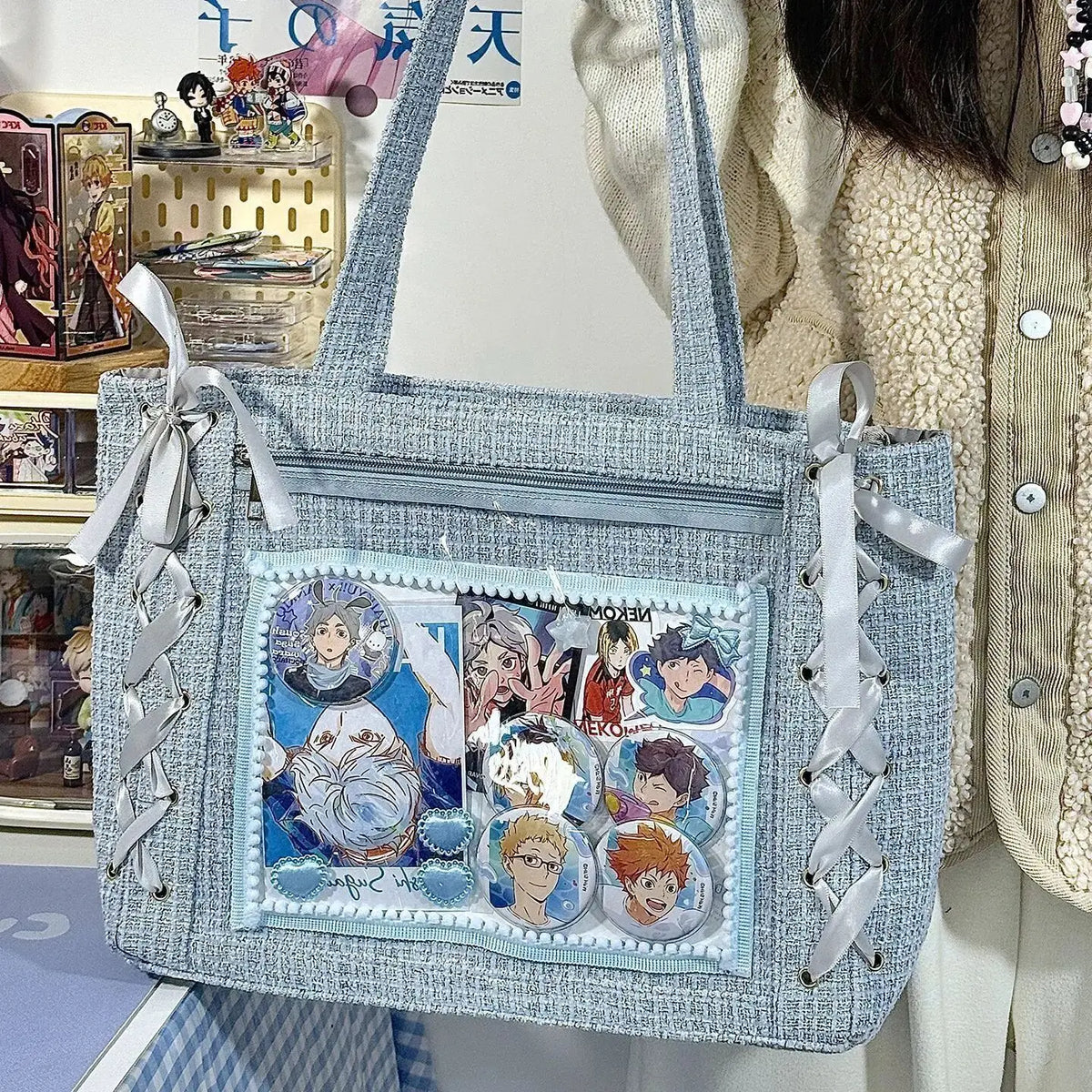 A light blue textured canvas tote bag with white ribbon details and a transparent window featuring various character illustra