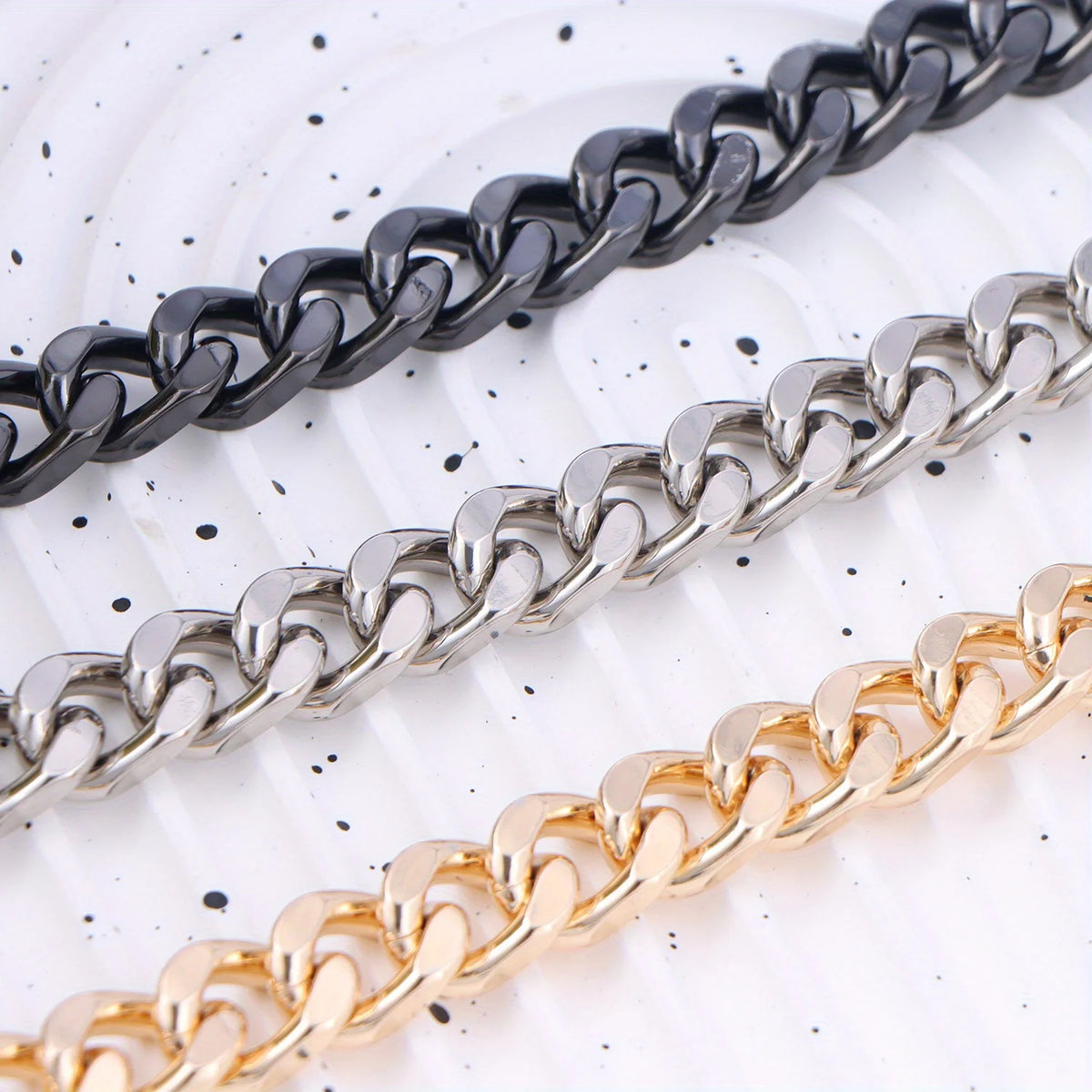 Three strands of heart-shaped metal purse chains in black, silver, and gold laid diagonally on a white background.