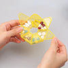 A hand holds a yellow weekly pill organizer divided into seven sections for daily medication.