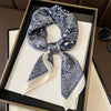 A blue and white paisley silk hair scarf tied in a bow, displayed in a black frame.