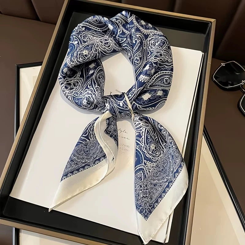 A blue and white paisley silk hair scarf tied in a bow, displayed in a black frame.
