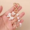 A gold-toned heart keychain featuring a pearl bow design, held in a person's hand.