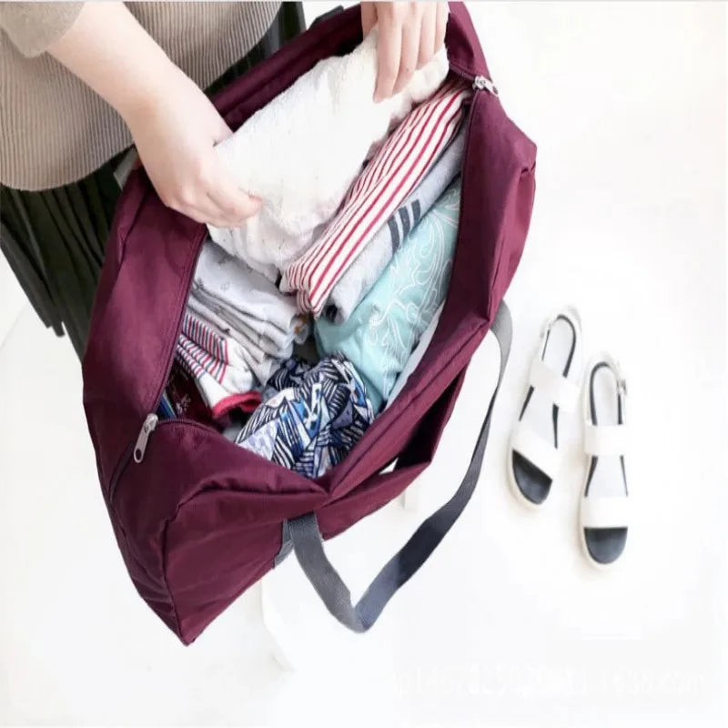 Une personne met des articles dans une valise de voyage pliable bordeaux, montrant des vêtements pliés et une serviette blanc