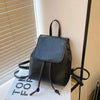 Mini sac à dos noir rétro marron avec cordon, exposé sur une surface blanche près d'un store