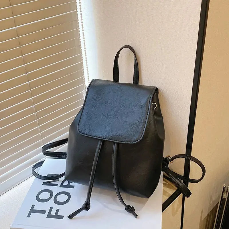 Mini sac à dos noir rétro marron avec cordon, exposé sur une surface blanche près d'un store