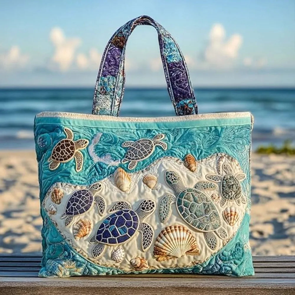 A turquoise quilted canvas tote bag featuring various sea turtle and shell embroidery on a wooden surface by the ocean.