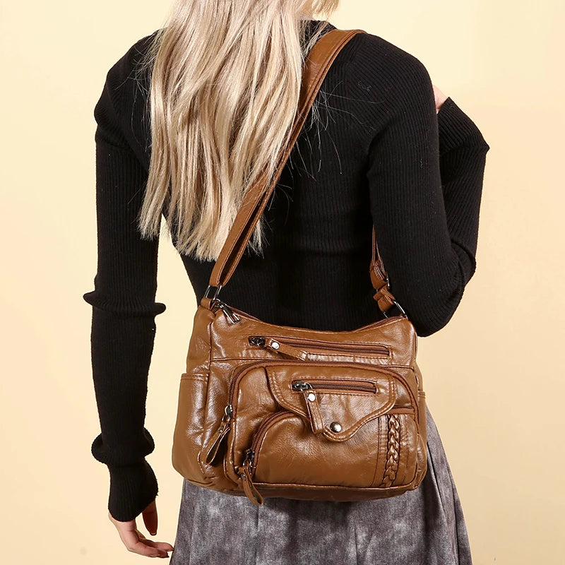 A woman is holding a brown leather tote bag with a tan strap against a light background.