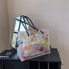 A clear plastic shoulder bag set with heart-shaped designs and a mirrored surface resting on a dark surface.