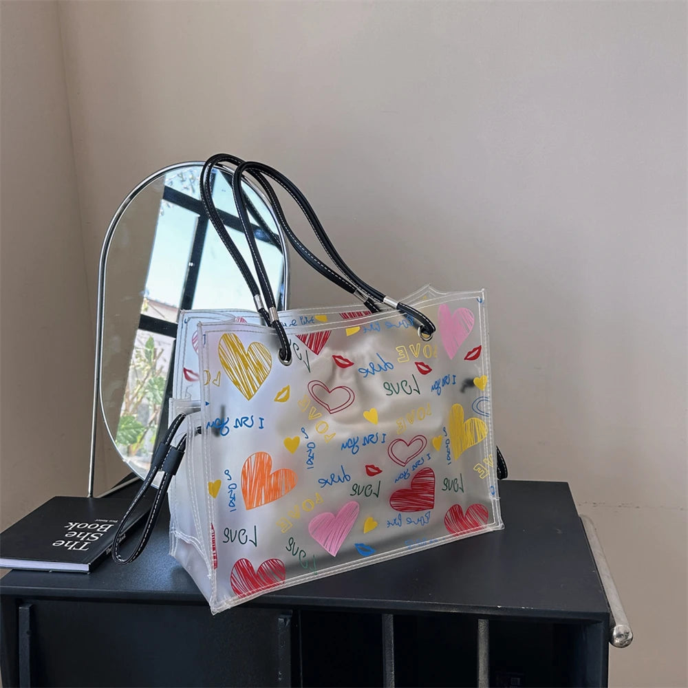 A clear plastic shoulder bag set with heart-shaped designs and a mirrored surface resting on a dark surface.