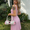 A woman models a pink dress and a polka dot bow shoulder bag outdoors.