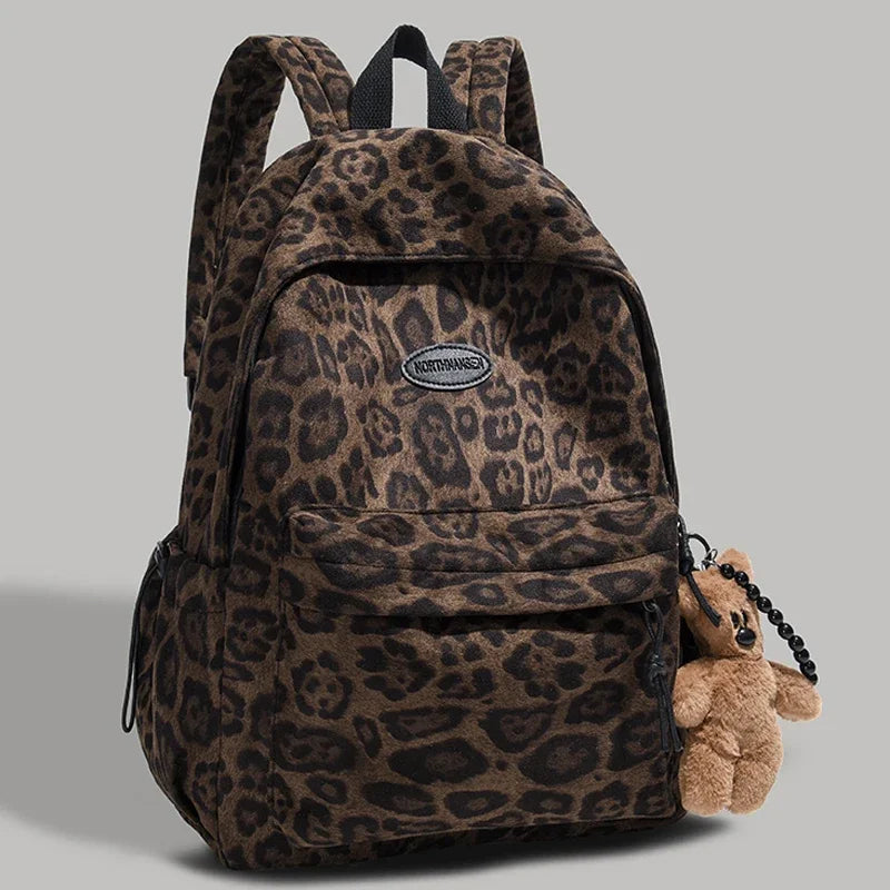 A brown leopard print backpack with black straps and a small teddy bear accessory.