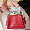 A red leather coin purse with a gold clasp and a stack of US currency is held by a person.
