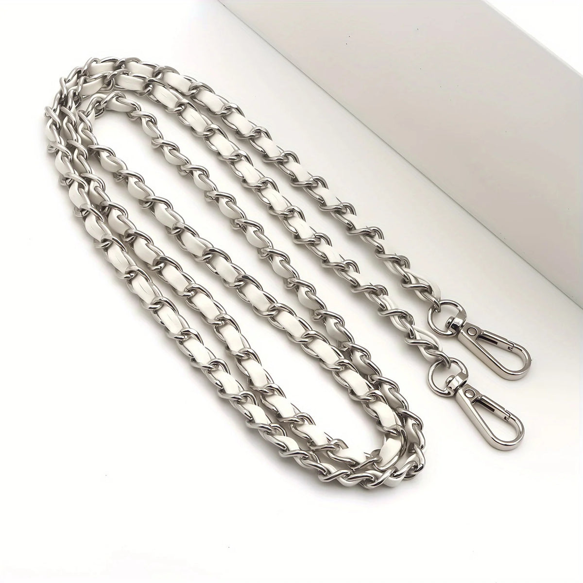 Silberne Metallkette als Trageriemen für eine Crossbody-Handtasche, diagonal auf weißem Untergrund.