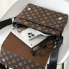 A brown patterned crossbody bag is placed on a white table next to a smartphone and sunglasses.