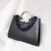 Black acrylic resin detachable bag chain strap on a black leather handbag set against a white fluffy background