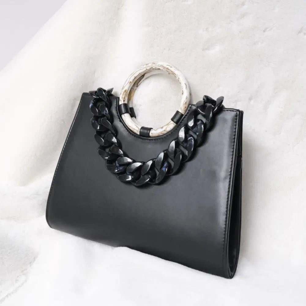 Black acrylic resin detachable bag chain strap on a black leather handbag set against a white fluffy background