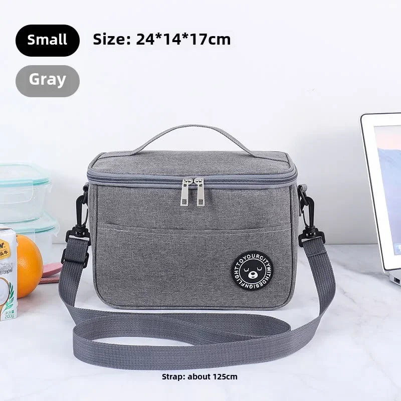 A gray insulated portable lunch bag with a strap is shown on a white marble surface.