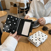 A black polka dot passport holder is shown on a wooden table next to a white polka dot wallet.