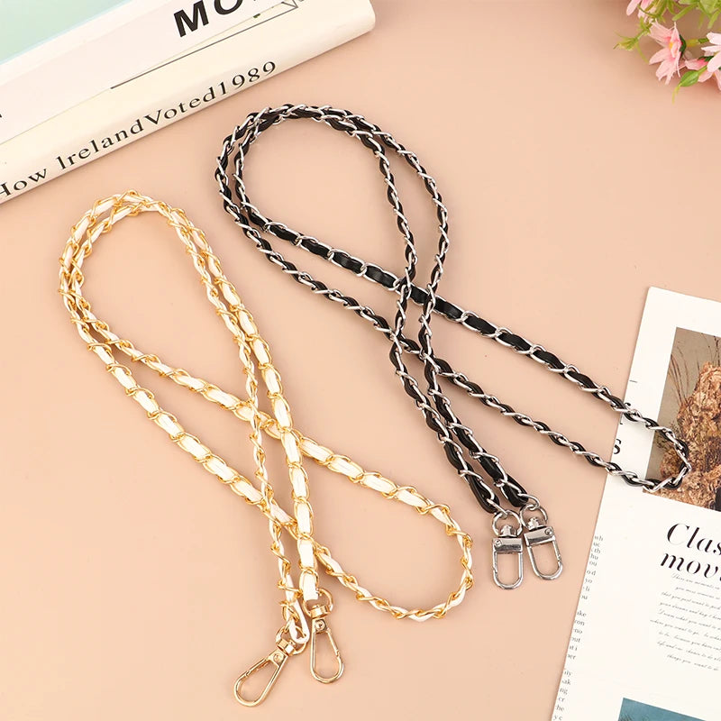 Two adjustable leather crossbody purse chain straps in gold and black lying on a light pink surface.