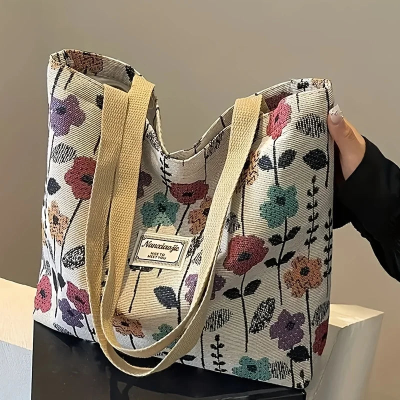 A beige bohemian corduroy tote bag with a floral pattern is held by a hand.