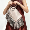 A woman holds a fringed Y2K clutch bag with tassel detail against a neutral background.