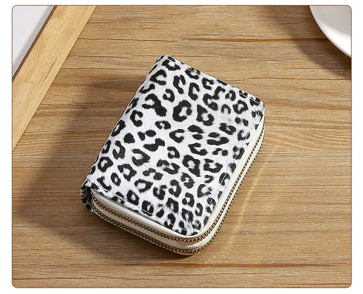 A small wallet with a leopard print fabric and a gold-toned zipper is placed on a wooden surface.