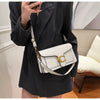 A woman holds a white textured shoulder bag with gold hardware against a black blazer.